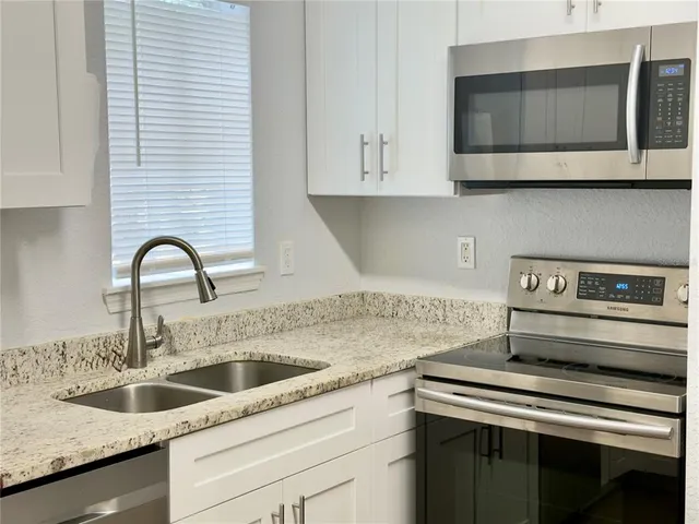 a kitchen with stainless steel appliances granite countertop a stove a sink and white cabinets with wooden floor