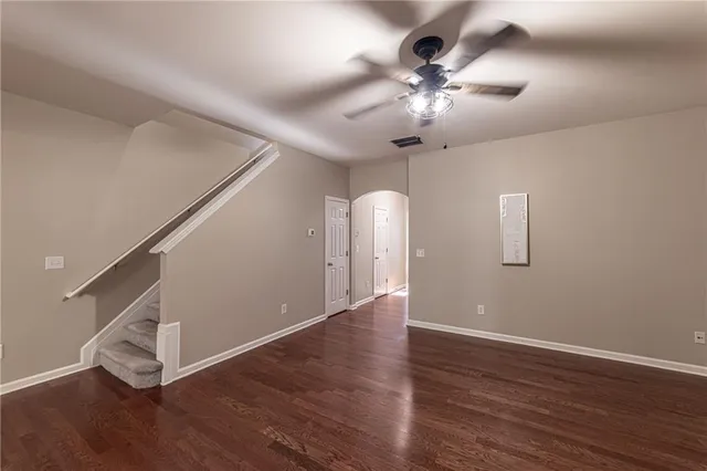 a view of an empty room with wooden floor a ceiling fan and windows