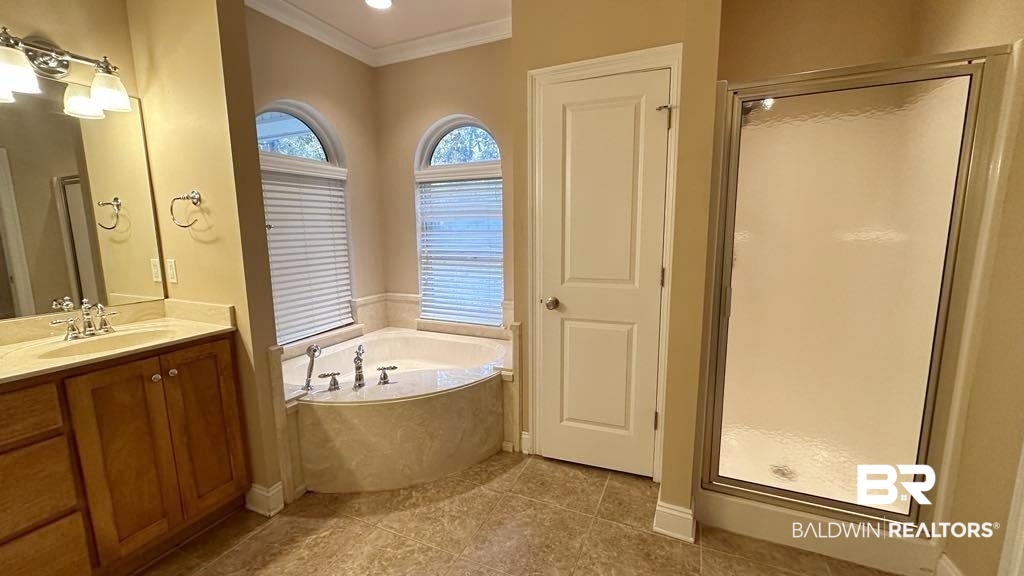 23289 McPhillips Road Loxley, AL 36551 - Photo 9 of 19 Bathroom featuring a corner soaking tub with arched windows, a glass-enclosed shower, wood-finish vanity with a single basin, and tiled flooring