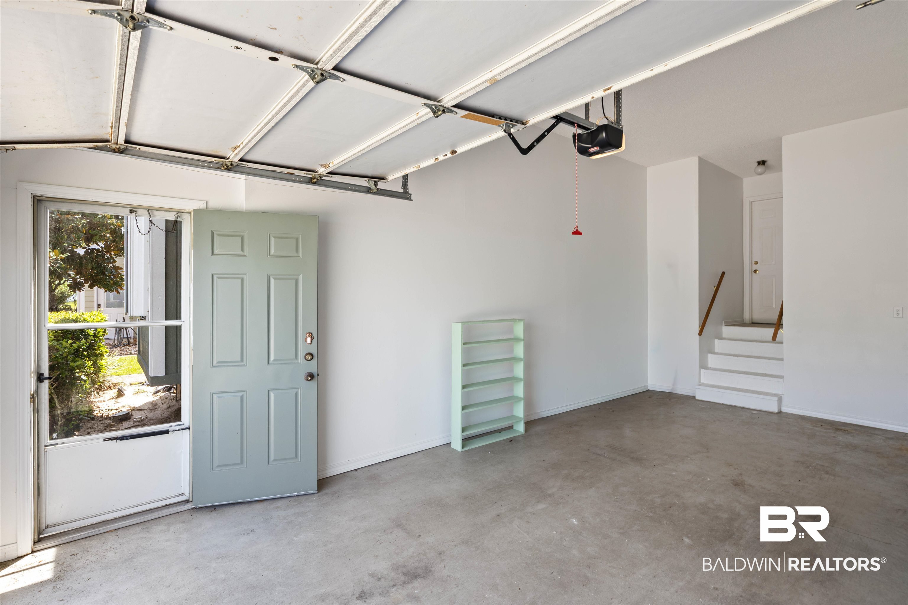 3200 Loop Road, Unit 96 Orange Beach, AL 36561 - Photo 9 of 49 Spacious garage featuring a concrete floor, overhead garage door mechanism, interior access door, and a multi-step staircase with a wooden handrail
