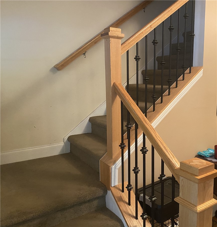 A classic wooden handrail paired with elegant metal balusters lines this carpeted staircase.