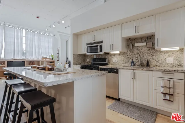 a kitchen with stainless steel appliances granite countertop a stove a sink a microwave a refrigerator and white cabinets