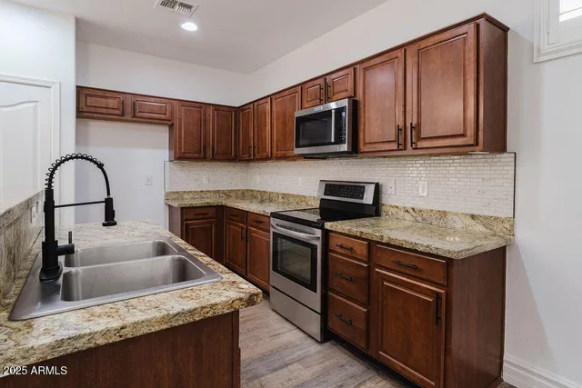 a kitchen with stainless steel appliances granite countertop a sink dishwasher stove and microwave with wooden cabinets