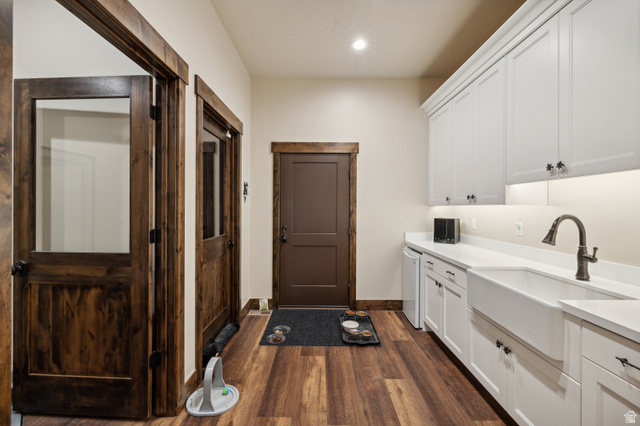 6117 North Rocky Ridge Road Peoa, UT 84061 - Photo 58 of 82 Utility space featuring wood-finish flooring, white cabinetry with dark hardware, a white farmhouse sink with a gooseneck faucet, light countertops, and dark wood trim around doors