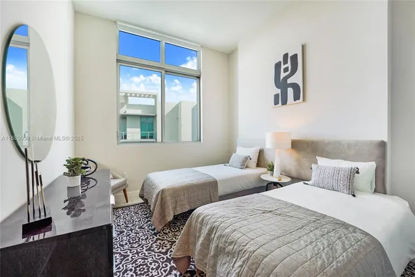 a bedroom with two beds and a large mirror next to a window