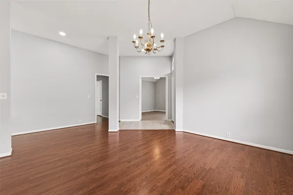 a view of an empty room with chandelier and wooden floor