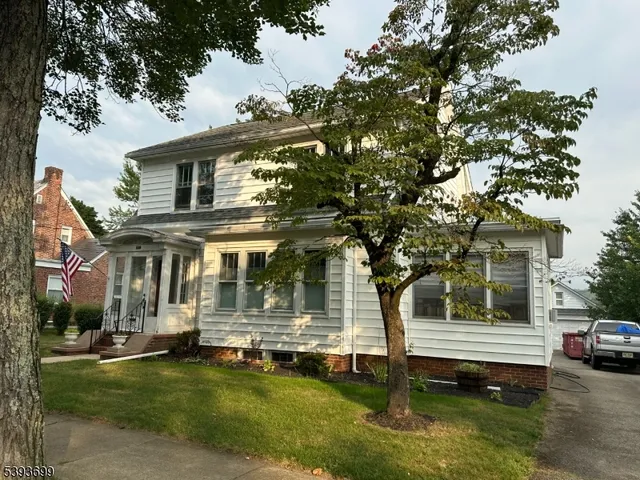 a view of a white house with a big yard plants and large trees