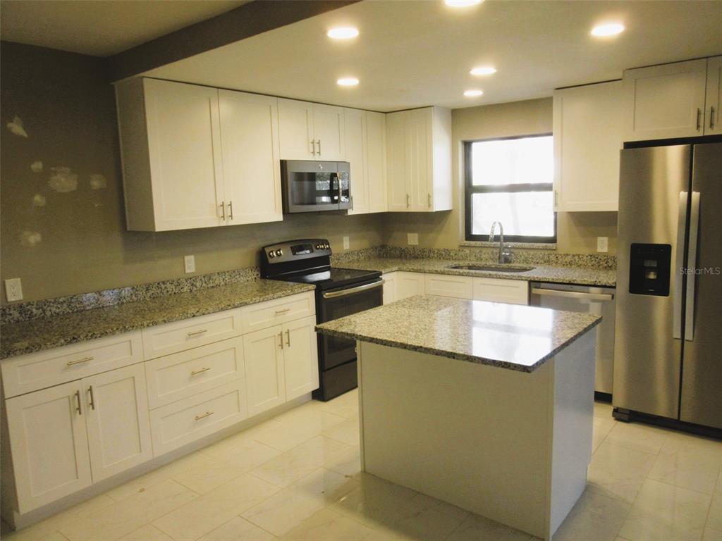 17455 Overhill Drive, Unit B Fort Myers, FL 33908 - Photo 5 of 13 a kitchen with stainless steel appliances granite countertop a stove a sink a refrigerator a microwave and white cabinets