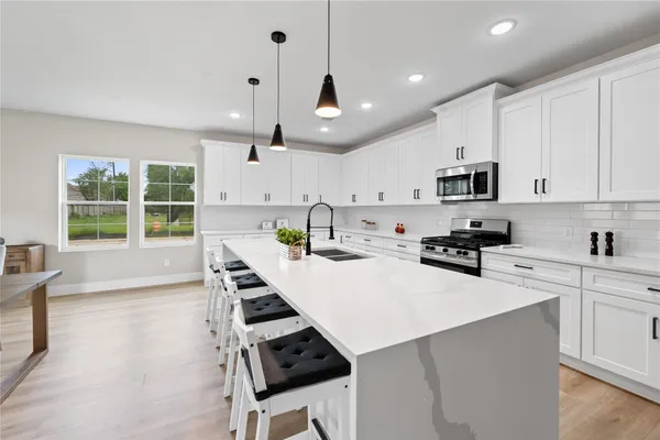 a kitchen with stainless steel appliances kitchen island granite countertop a sink a stove a refrigerator cabinets and a dining table with wooden floor