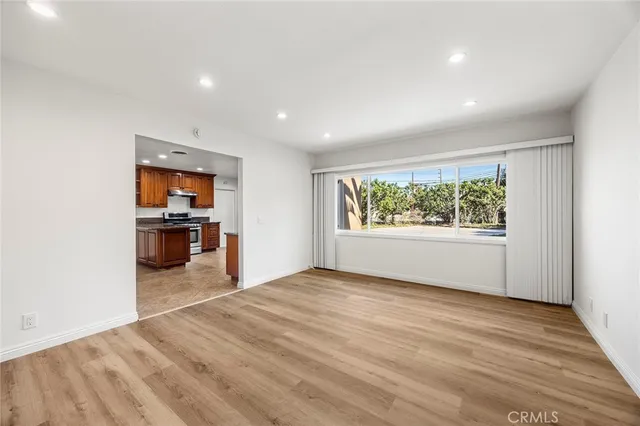 an empty room with wooden floor kitchen view and a window