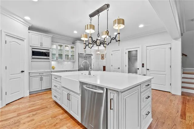 a large white kitchen with stainless steel appliances granite countertop a stove oven a sink dishwasher and white cabinets with wooden floor