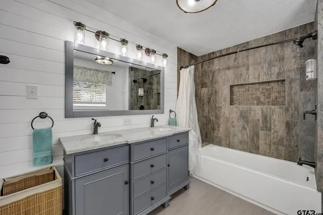 a bathroom with a granite countertop sink a mirror a bathtub and shower