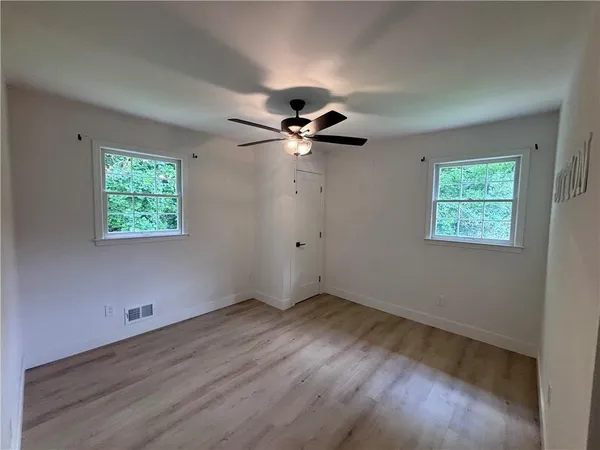 a view of an empty room with wooden floor and a ceiling fan