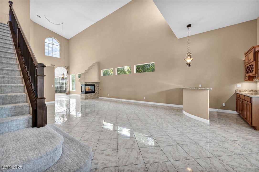 2107 Eaglepath Circle Henderson, NV 89074 - Photo 43 of 84 Living area featuring high vaulted ceiling, light marble finish flooring, a multi sided fireplace, stairs, and a chandelier