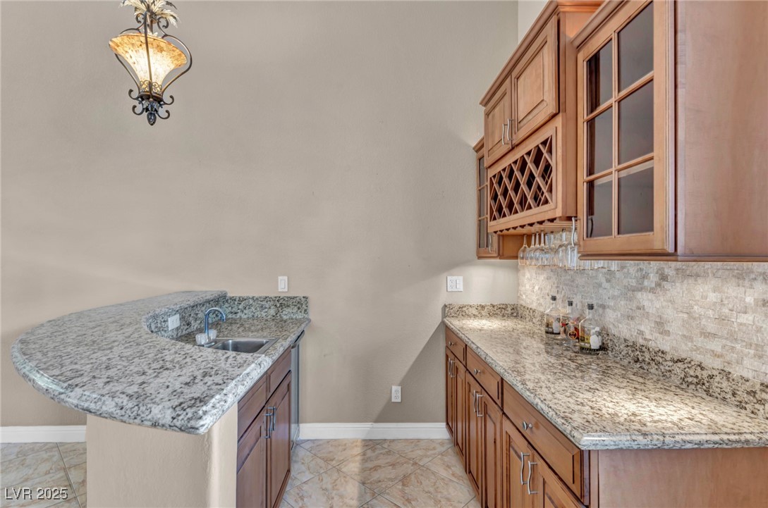 2107 Eaglepath Circle Henderson, NV 89074 - Photo 44 of 84 Kitchen with a peninsula, brown cabinets, glass insert cabinets, and light stone countertops