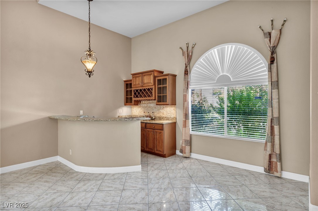 2107 Eaglepath Circle Henderson, NV 89074 - Photo 5 of 84 Bar with brown cabinetry, decorative light fixtures, light stone counters, and glass insert cabinets