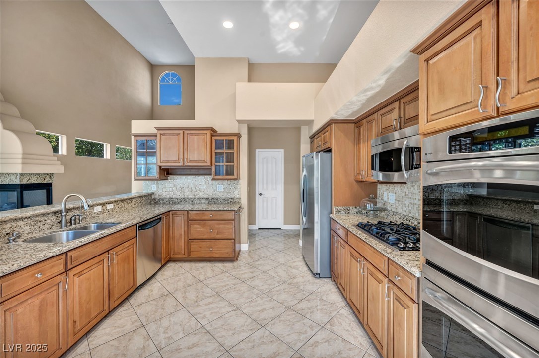 2107 Eaglepath Circle Henderson, NV 89074 - Photo 6 of 84 Kitchen with stainless steel appliances, brown cabinetry, decorative backsplash, light stone countertops, and a high ceiling