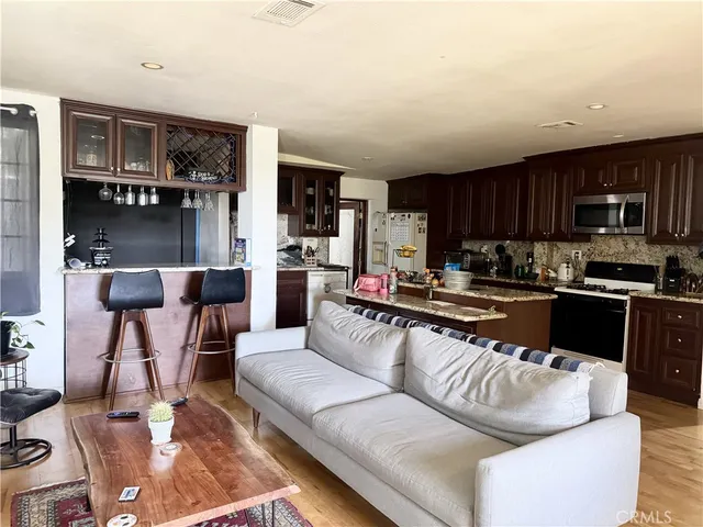 a living room with stainless steel appliances furniture a rug and a kitchen view