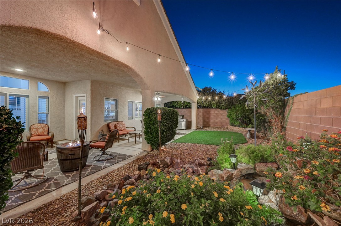 1604 Cattle Ranch Place Henderson, NV 89002 - Photo 8 of 99 A tranquil backyard oasis features a covered patio, a fire pit, and a vibrant garden under string lights.