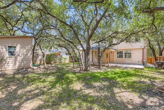 a backyard of a house with large trees and wooden fence