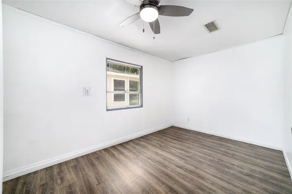 an empty room with wooden floor chandelier fan and windows