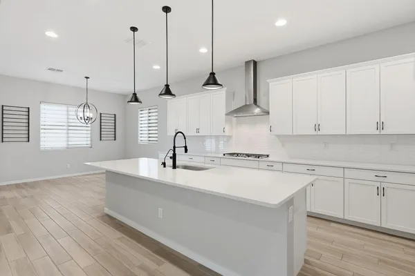 a kitchen with stainless steel appliances sink a stove and white cabinets with wooden floor