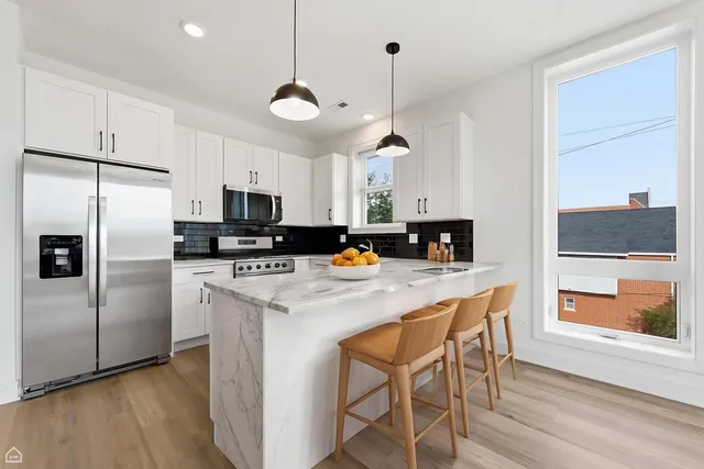 a kitchen with stainless steel appliances granite countertop a stove a refrigerator a microwave a sink a dining table and chairs with wooden floor