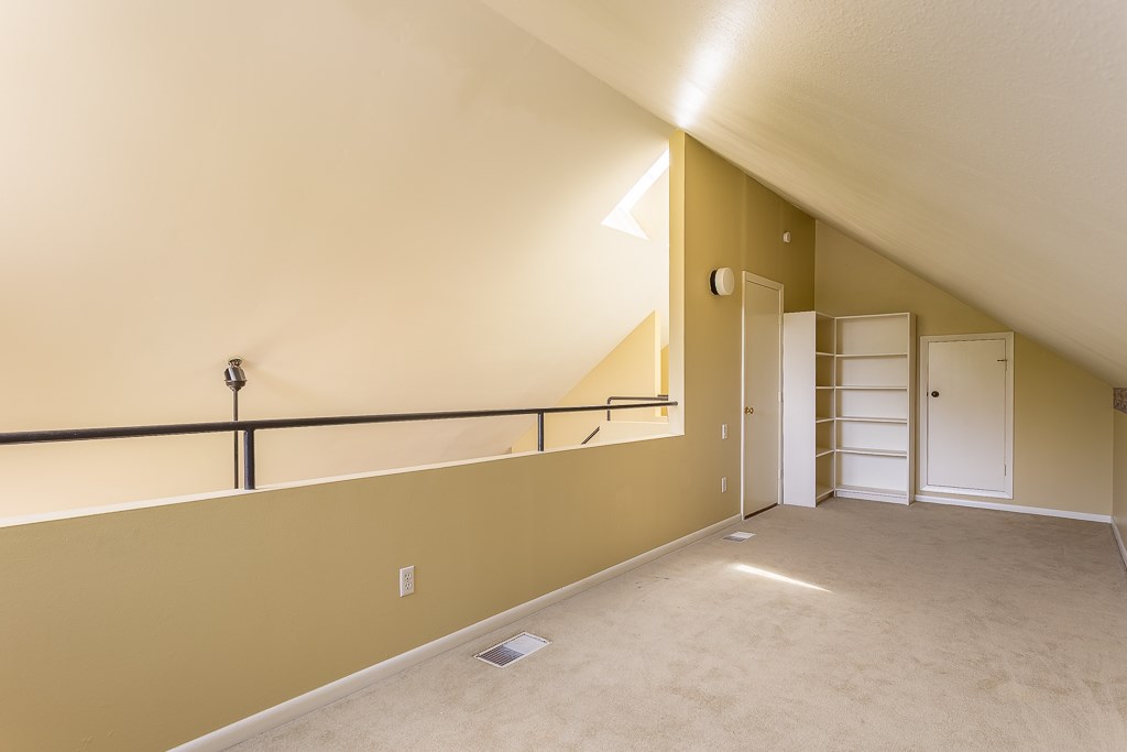 2349 Albans Road, Unit 2 Houston, TX 77005 - Photo 23 of 25 Spacious loft area with sloped ceilings, neutral carpet, and built-in shelving. It features a railing overlooking the lower level and a small window for natural light, ideal for a cozy reading nook or office space.