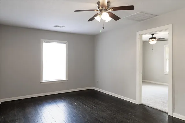 an empty room with wooden floor fan and windows