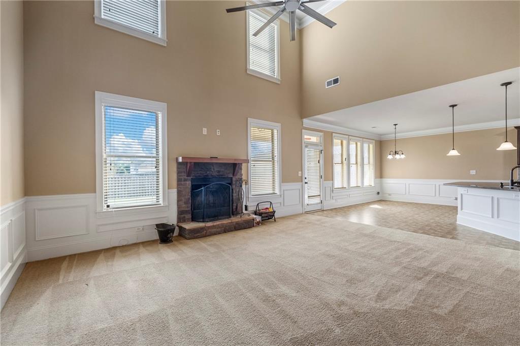 12 Juno Street Fort Mitchell, AL 36856 - Photo 6 of 43 Unfurnished living room with a decorative wall, a wainscoted wall, light carpet, a stone fireplace, and a high ceiling