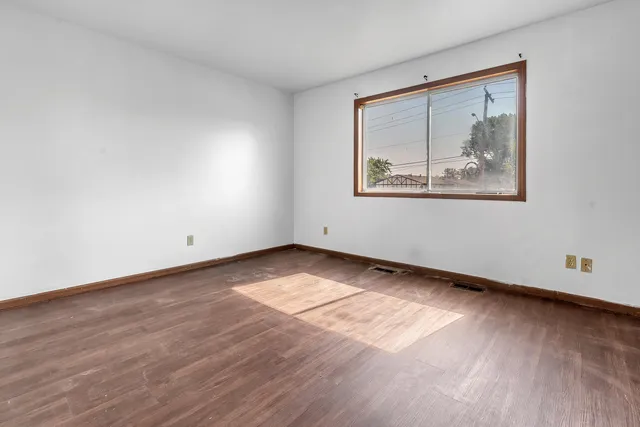 a view of an empty room with wooden floor and a window