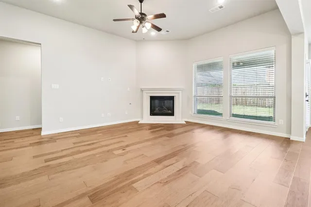 an empty room with wooden floor ceiling fan and windows