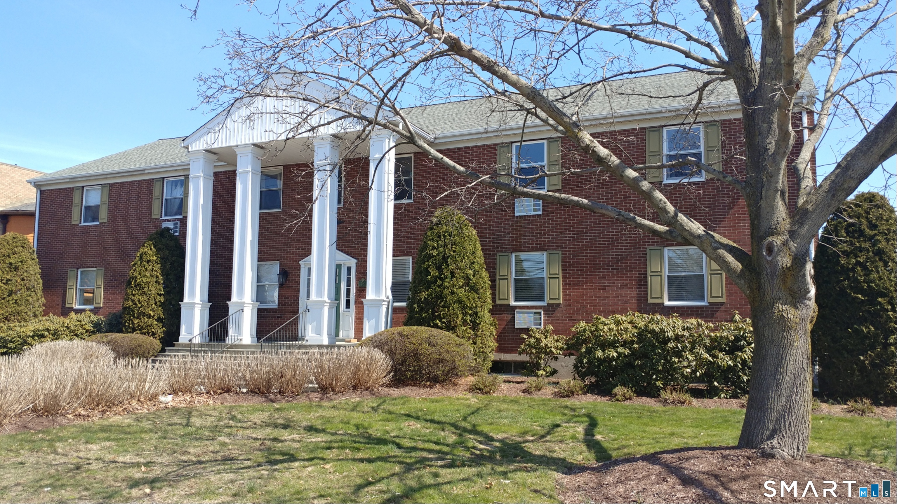 a view of a white house next to a yard with big trees