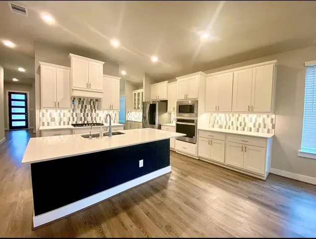 a room with kitchen island a sink wooden floor and stainless steel appliances