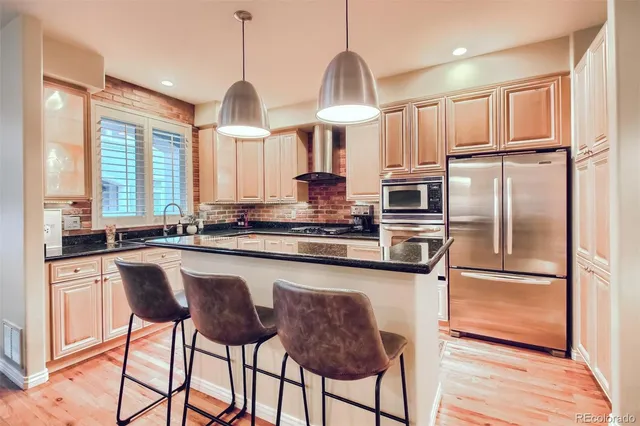 a kitchen with stainless steel appliances granite countertop a refrigerator a sink dishwasher a stove and white cabinets with wooden floor