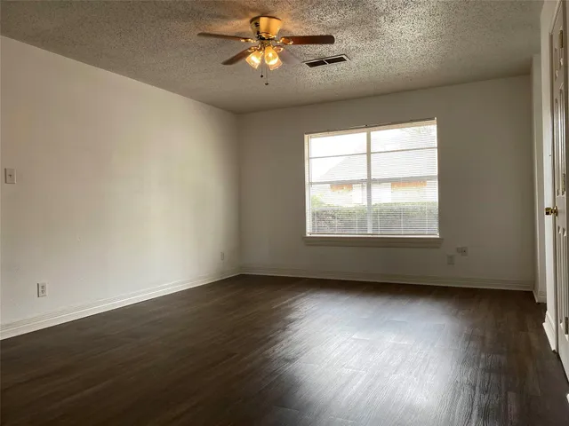 an empty room with wooden floor fan and windows