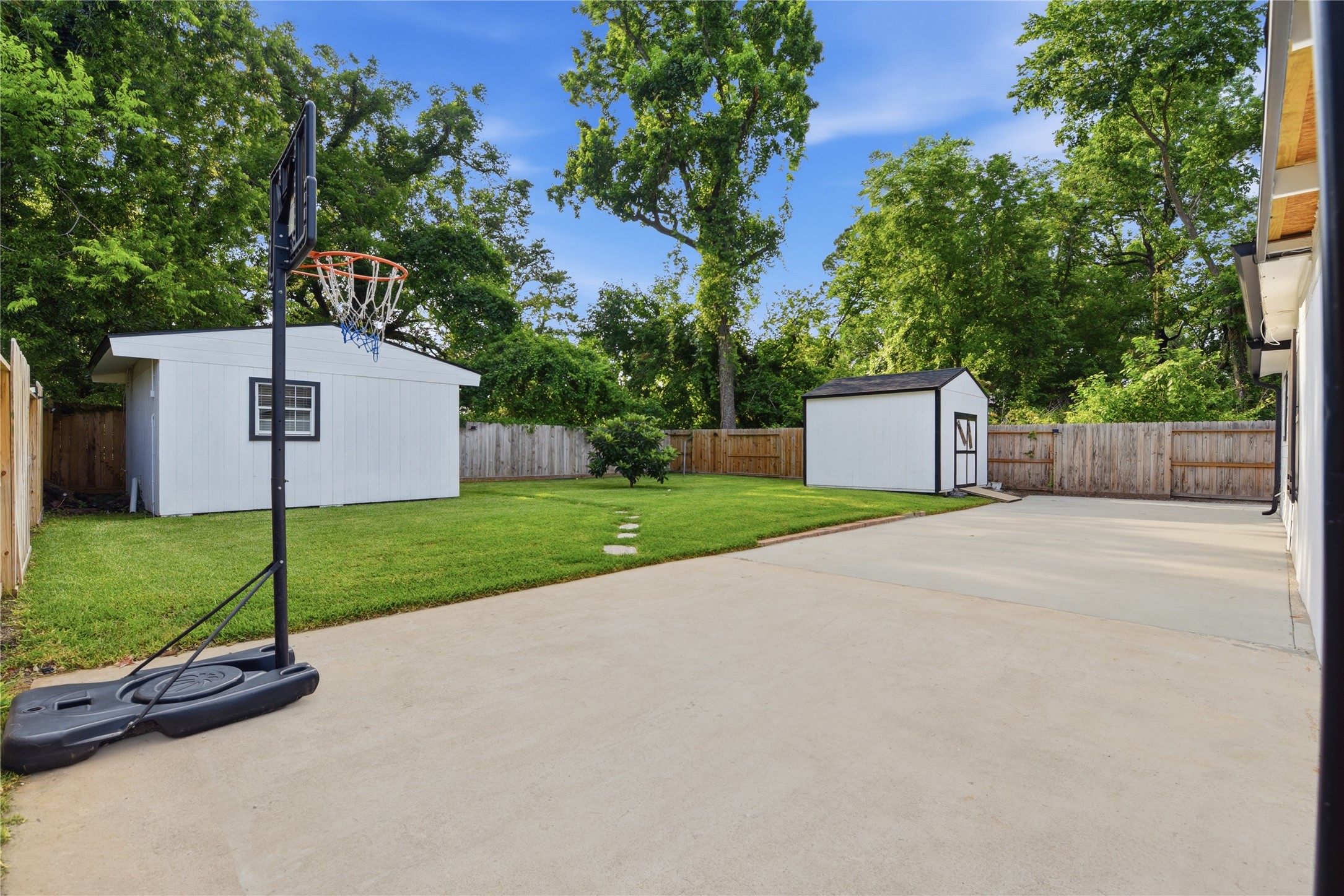 9403 Spaulding Street Houston, TX 77016 - Photo 6 of 50 Spacious backyard featuring a basketball hoop, two storage sheds, and a well-maintained lawn, all enclosed by a wooden fence.