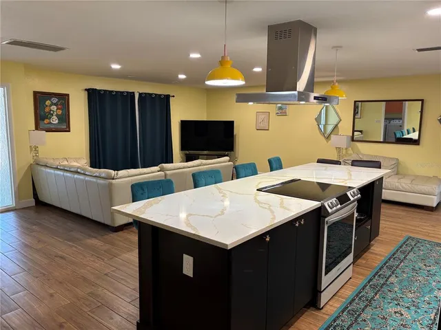 a kitchen with stainless steel appliances kitchen island granite countertop a sink a microwave oven and a dining table with wooden floor