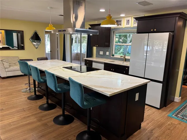 a kitchen with stainless steel appliances kitchen island granite countertop a table chairs and a refrigerator