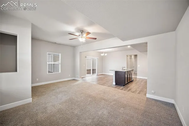 a view of an empty room with chandelier fan and wooden floor