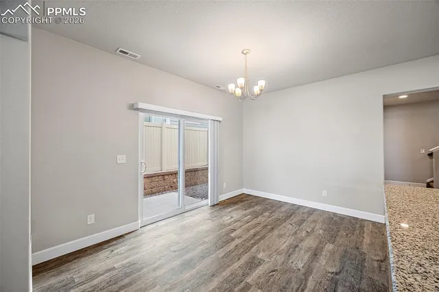 an empty room with wooden floor chandelier and windows