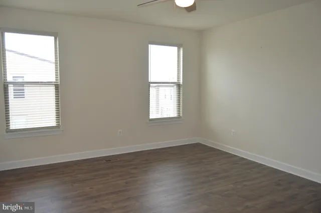 an empty room with wooden floor chandelier fan and windows