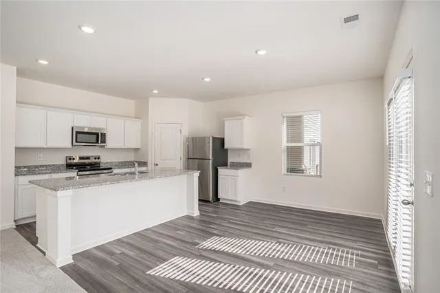 a kitchen with stainless steel appliances granite countertop a stove top oven a sink a refrigerator and white cabinets with wooden floor