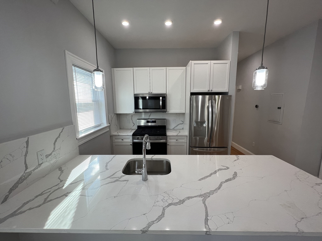 29 Alpine Street, Unit 1 Somerville, MA 02144 - Photo 5 of 33 a kitchen with stainless steel appliances kitchen island granite countertop a refrigerator a sink a stove with white cabinets