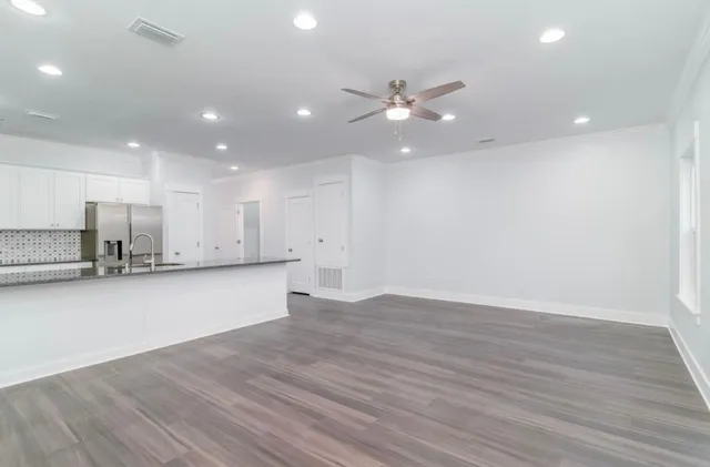 a view of an empty room with wooden floor and a ceiling fan