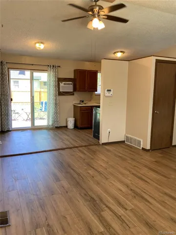 an empty room with wooden floor a flat screen tv and kitchen view