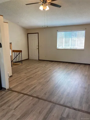 an empty room with wooden floor chandelier fan and windows