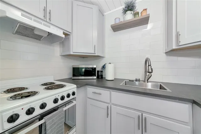 a white kitchen with stainless steel appliances granite countertop a stove and a microwave