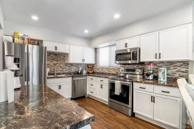 a kitchen with stainless steel appliances granite countertop a stove top oven a refrigerator a sink and dishwasher with white cabinets