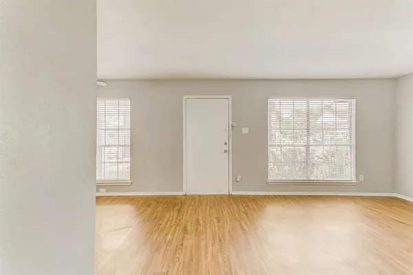 an empty room with wooden floor and windows with curtains